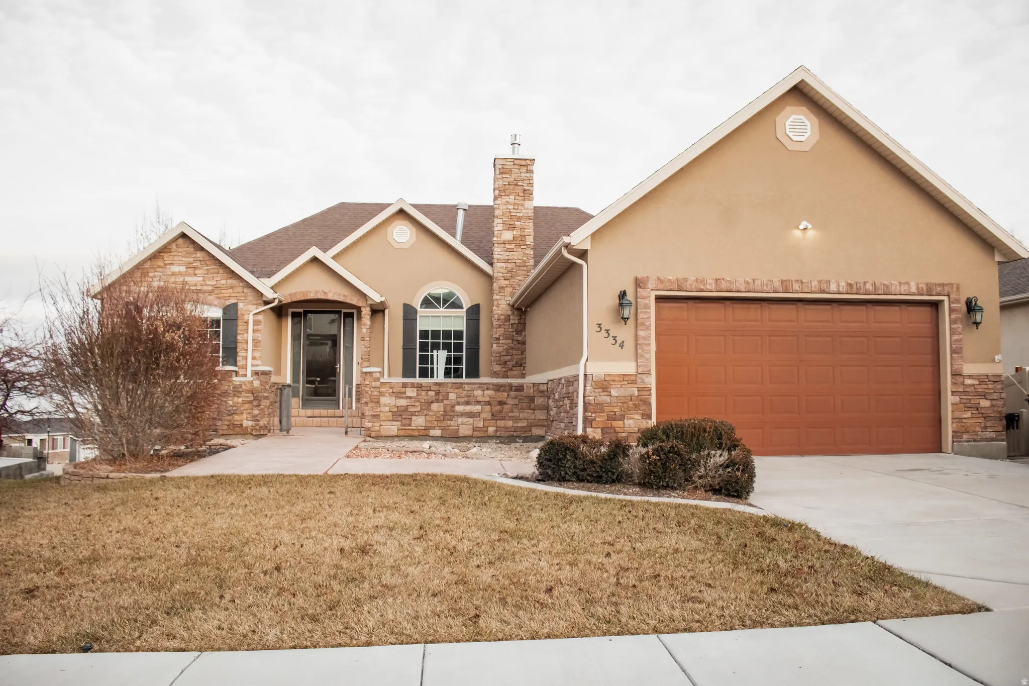 View of front of property with stucco siding, a front yard, stone siding, concrete driveway, and a garage