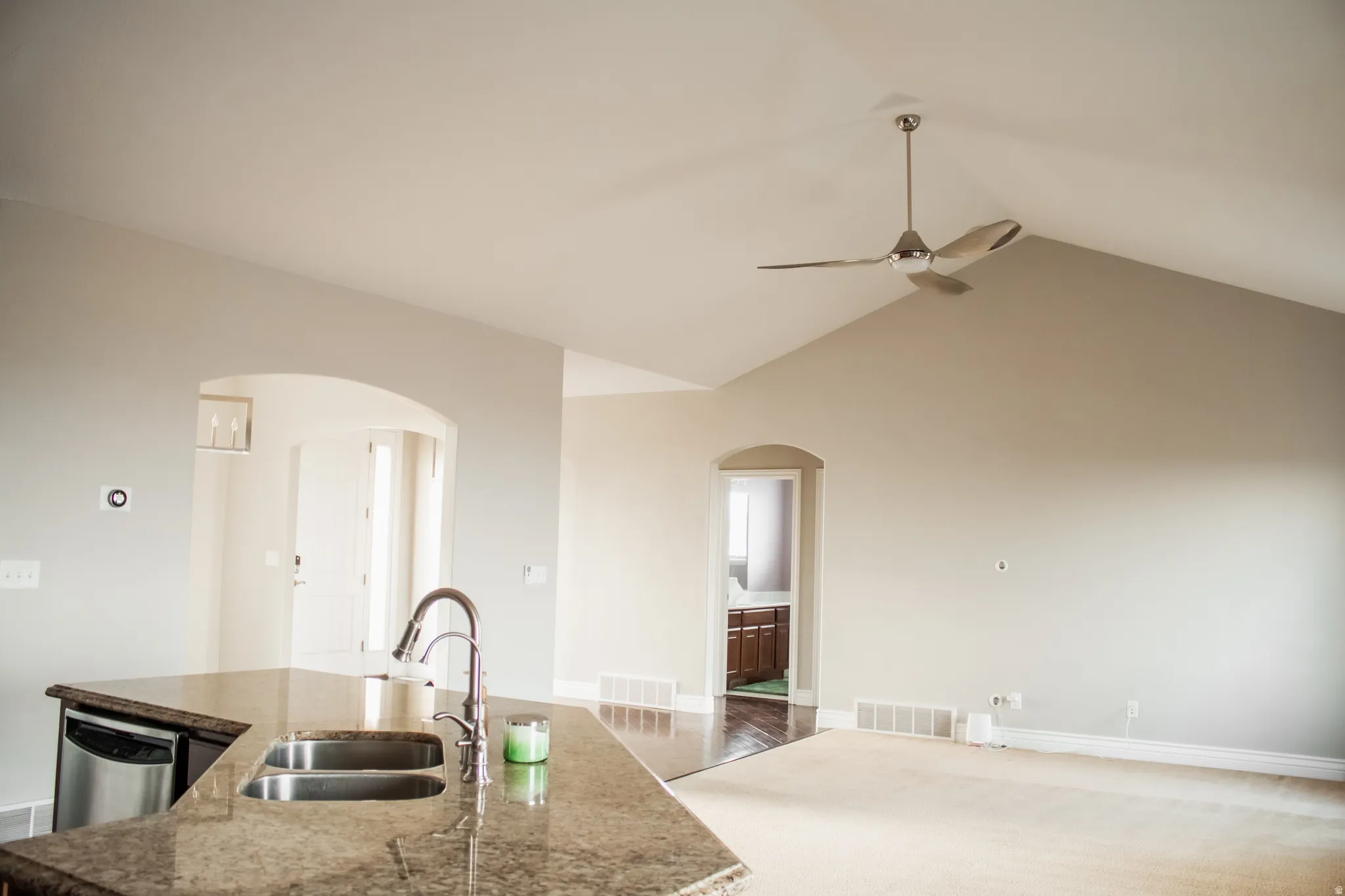 Kitchen featuring an island with sink, lofted ceiling, stainless steel dishwasher, dark stone countertops, and carpet