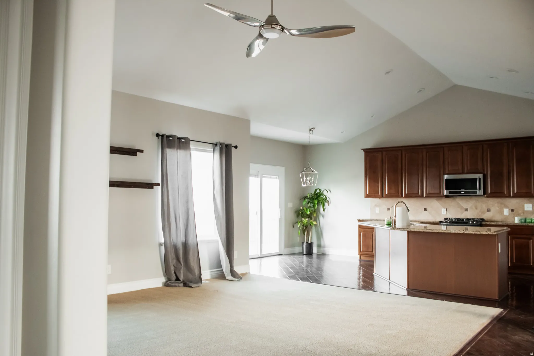 Kitchen with stainless steel microwave, light stone countertops, ceiling fan, a center island with sink, and tasteful backsplash