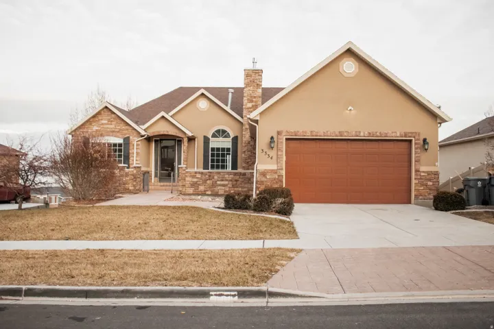View of front of house featuring stucco siding, driveway, stone siding, an attached garage, and a chimney