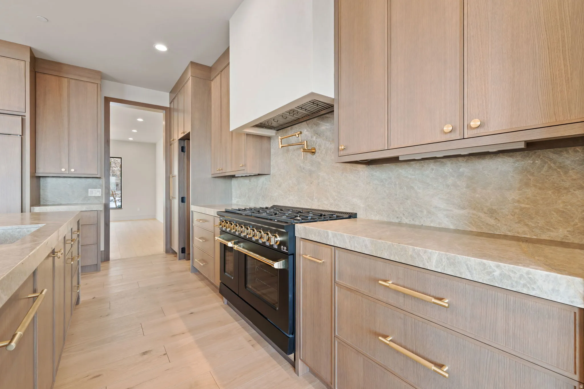 Primary Kitchen featuring designer gas range plaster range hood, Mojave quartzite countertops and backsplash and European White Oak floors.