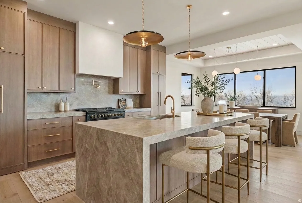 Primary Kitchen featuring decorative light fixtures, a kitchen breakfast bar, tasteful backsplash, light wood finished floors, and light stone countertops