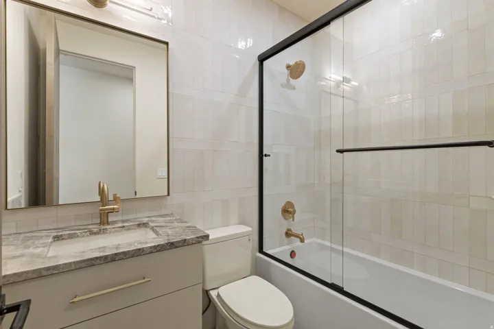 Ensuite bathroom  for bedroom 4 with bath / shower combo with glass door, vanity, and tile walls