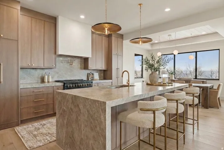 Primary Kitchen featuring decorative light fixtures, a kitchen breakfast bar, tasteful backsplash, light wood finished floors, and light stone countertops