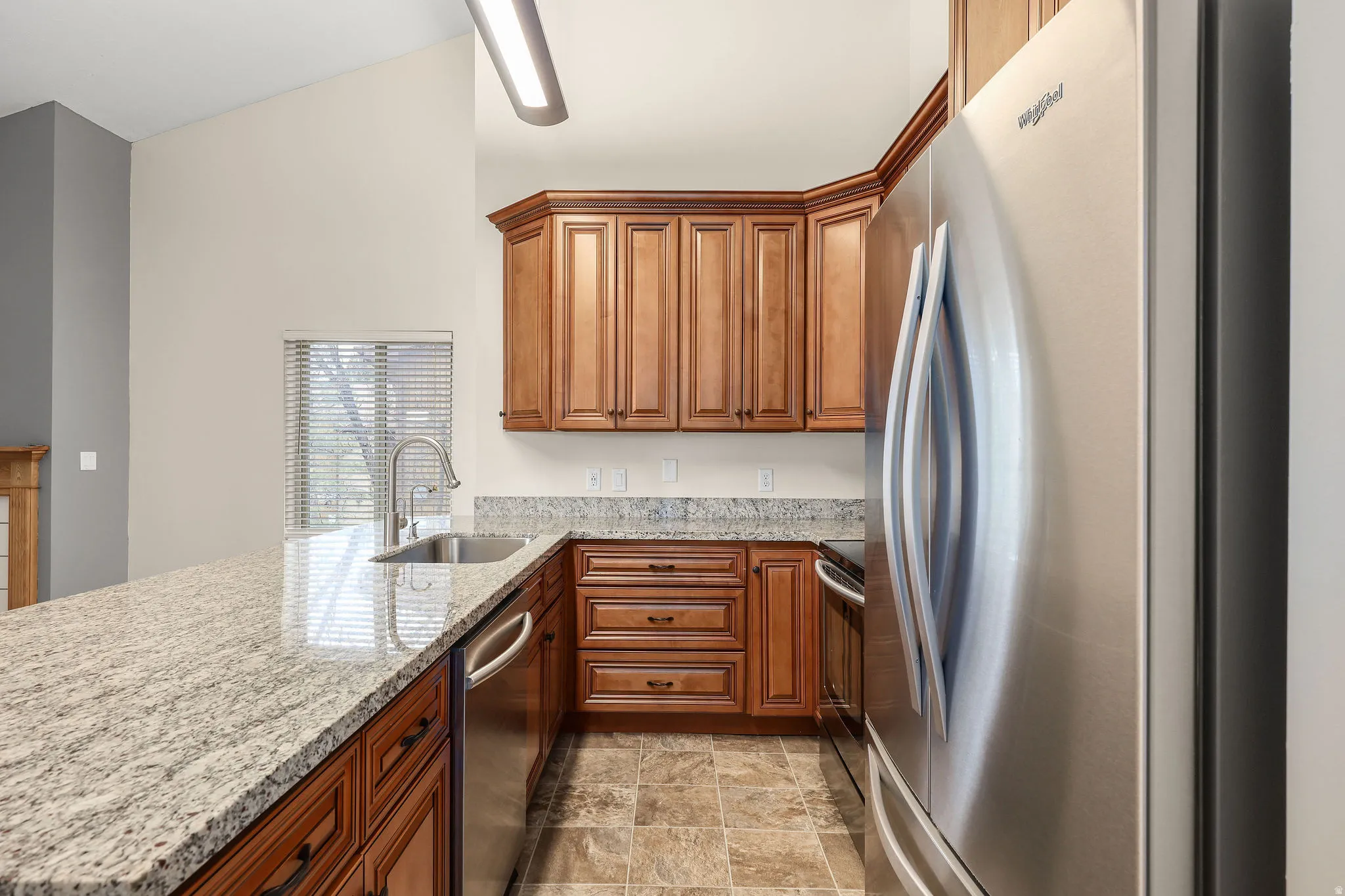 Kitchen featuring stainless steel appliances, wood finish cabinetry, light stone counters, a peninsula, and stone finish flooring