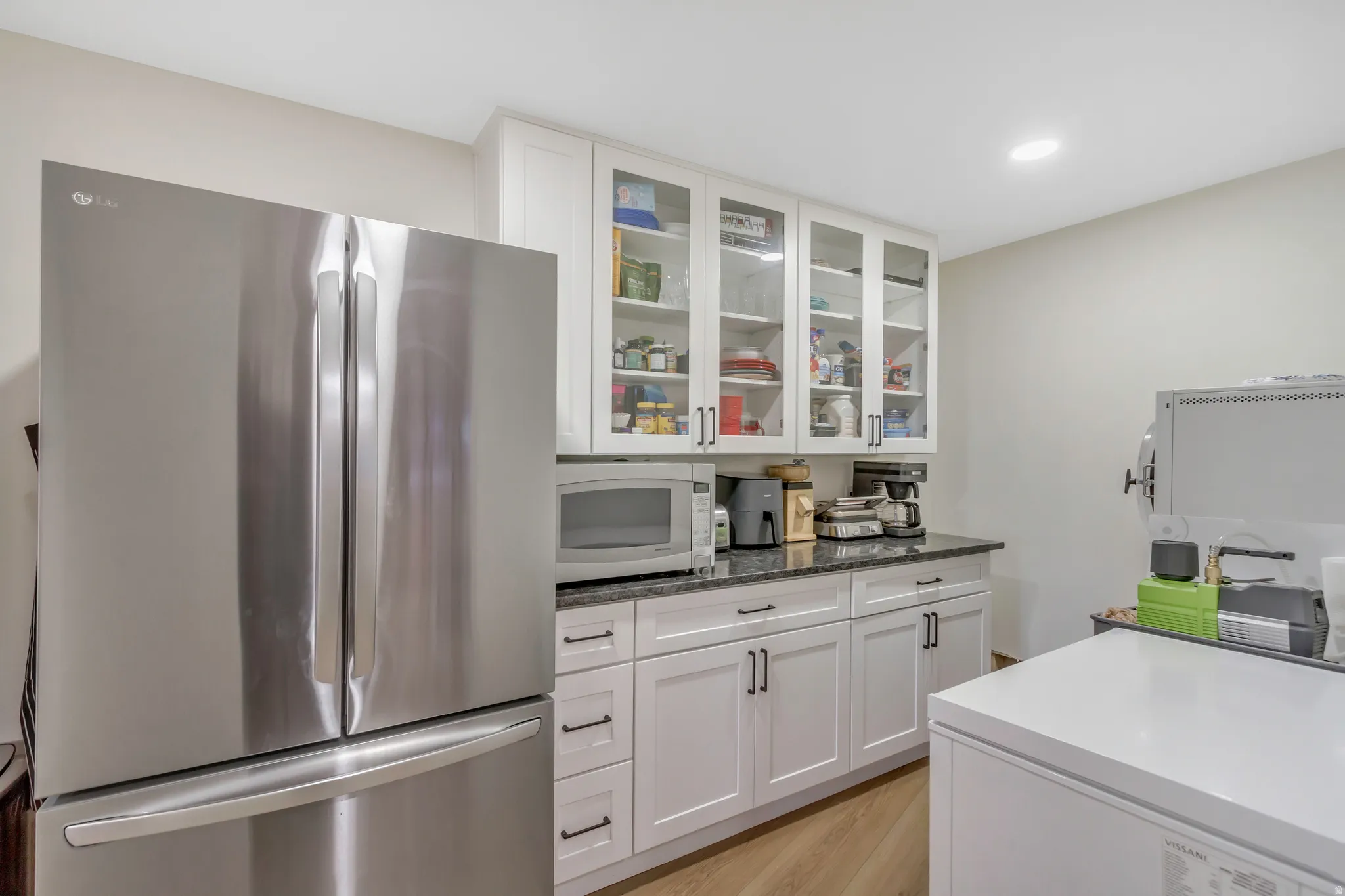 Kitchen featuring freestanding refrigerator, white cabinetry, white microwave, glass insert cabinets, and light wood-type flooring