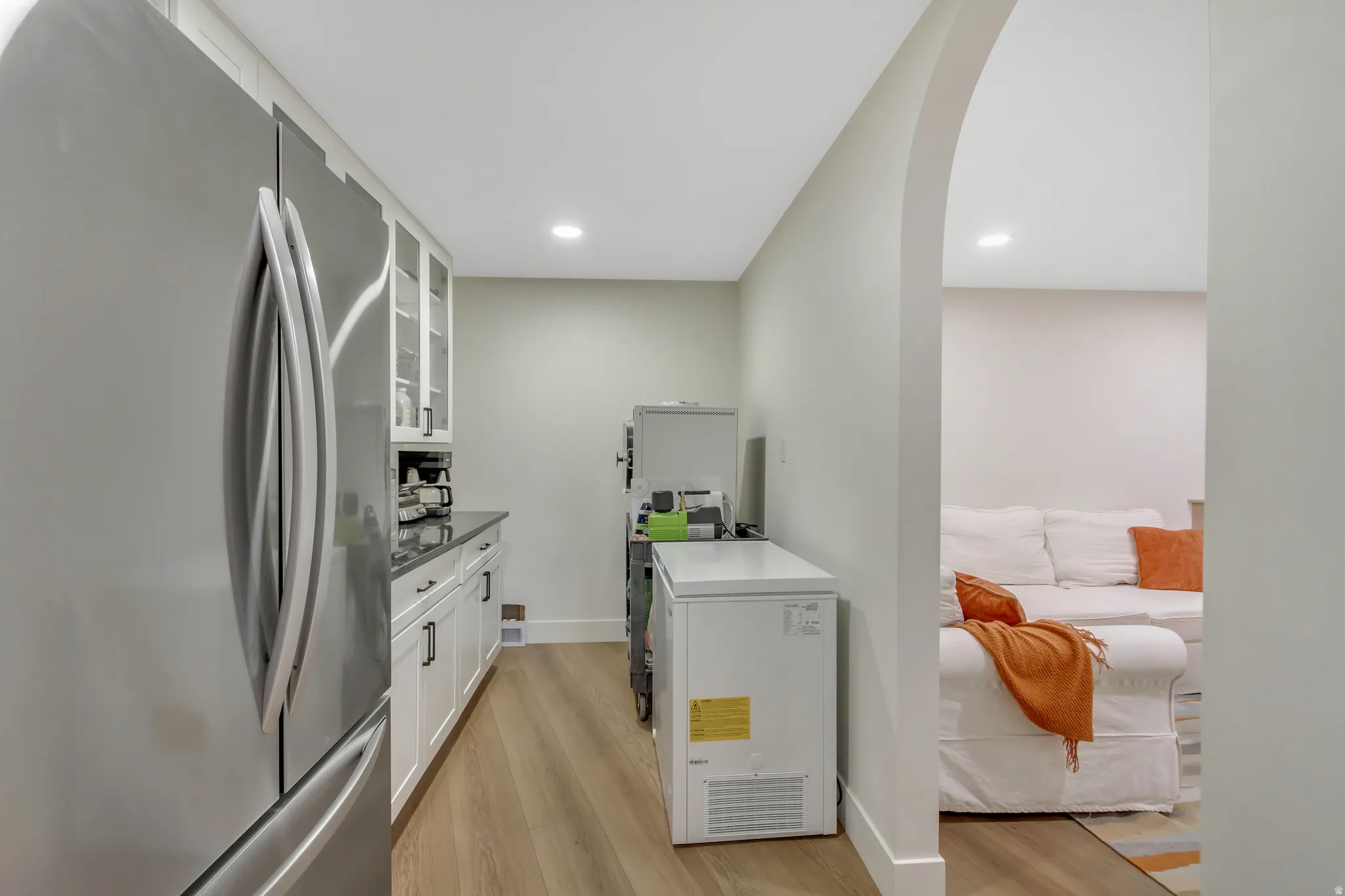 Kitchen featuring freestanding refrigerator, glass insert cabinets, white cabinets, arched walkways, and light wood finished floors
