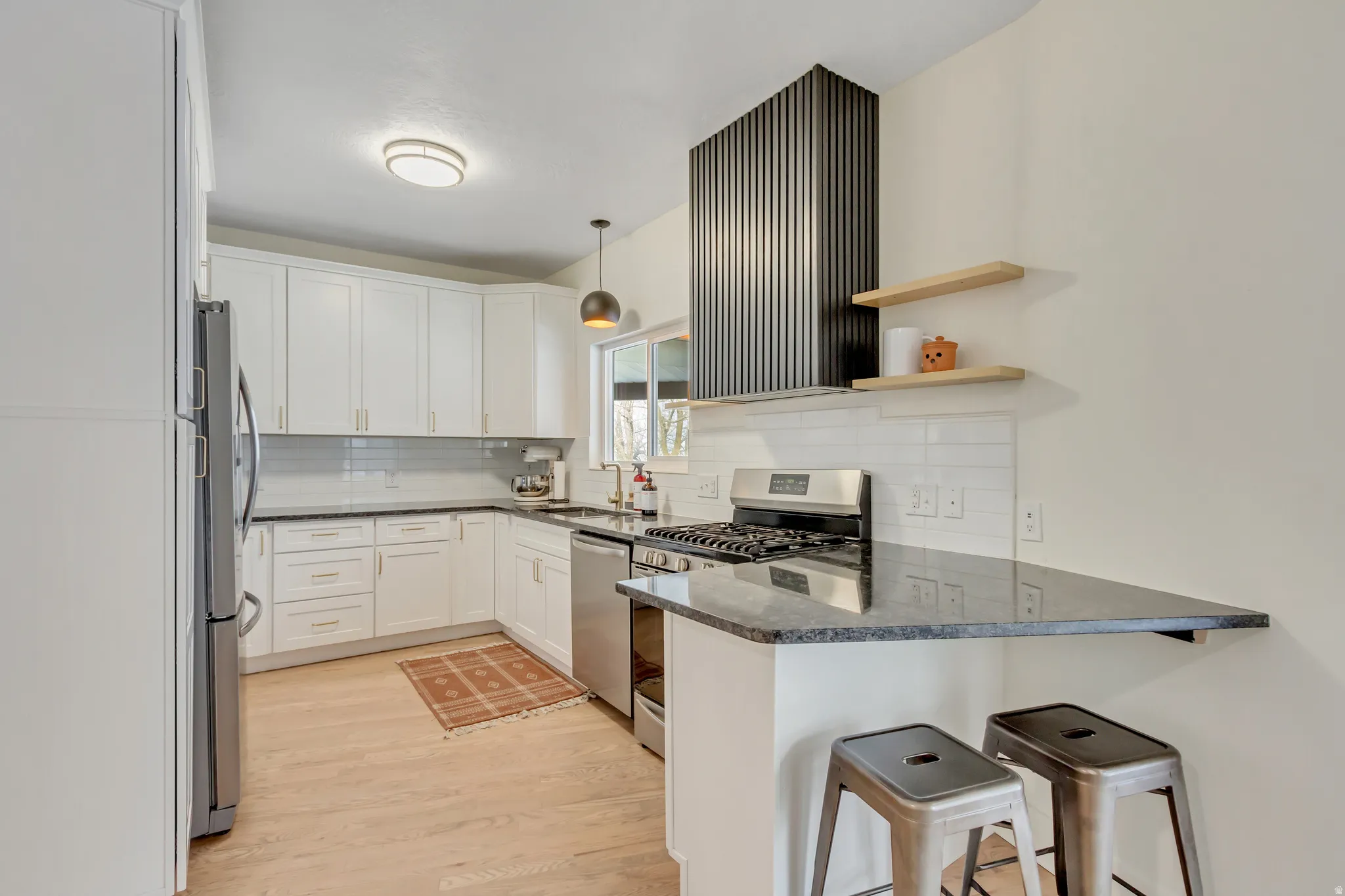 Kitchen featuring stainless steel appliances, a peninsula, dark stone countertops, light wood finished floors, and a kitchen bar
