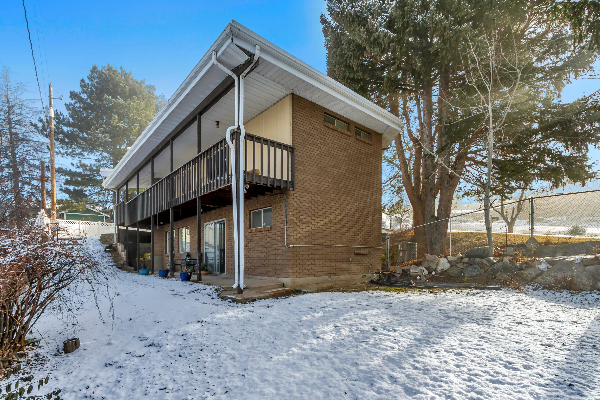 Snow covered back of property featuring a patio, brick siding, and a wooden deck