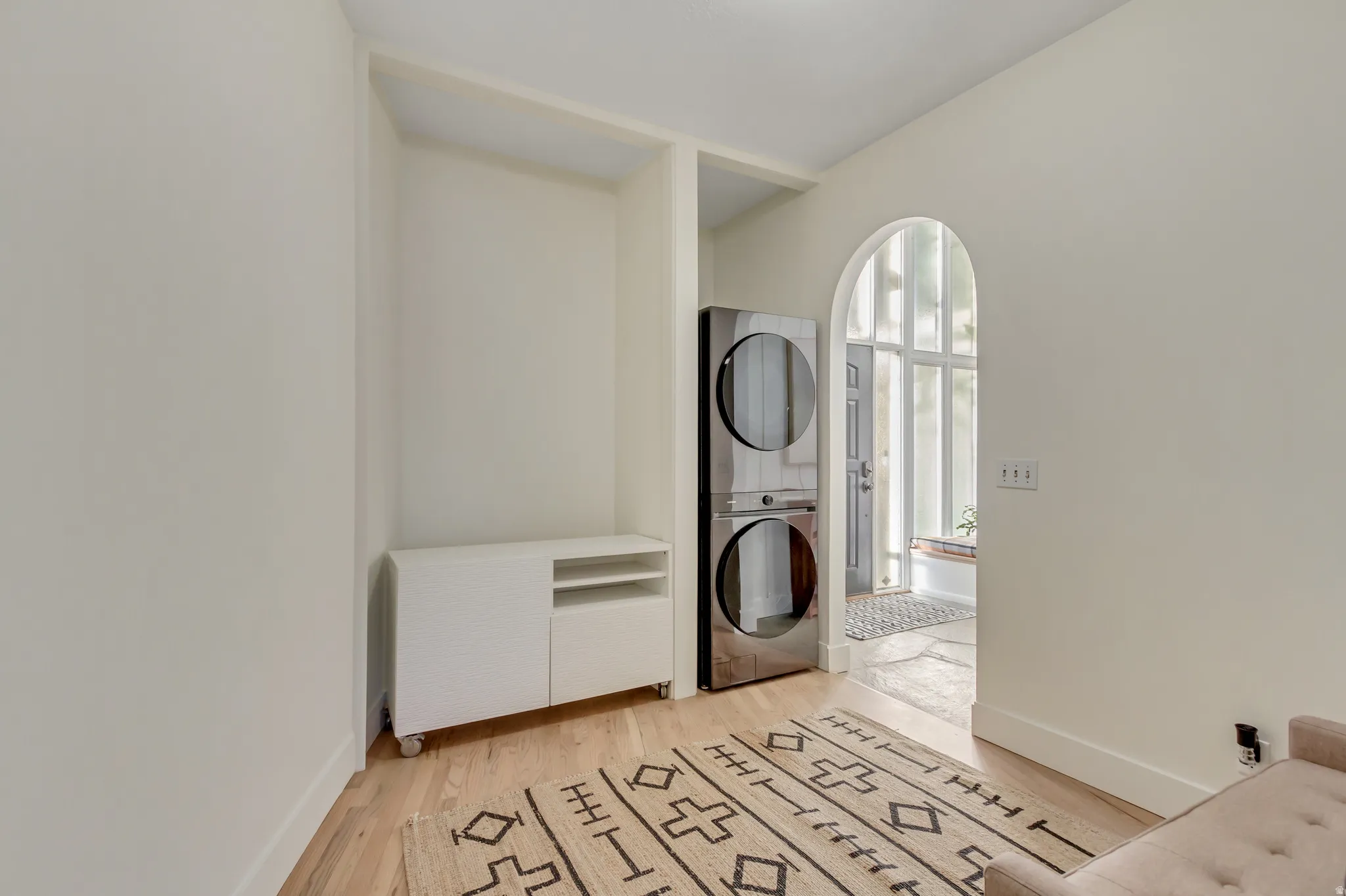 Laundry room with light wood-style floors and stacked washing machine and dryer