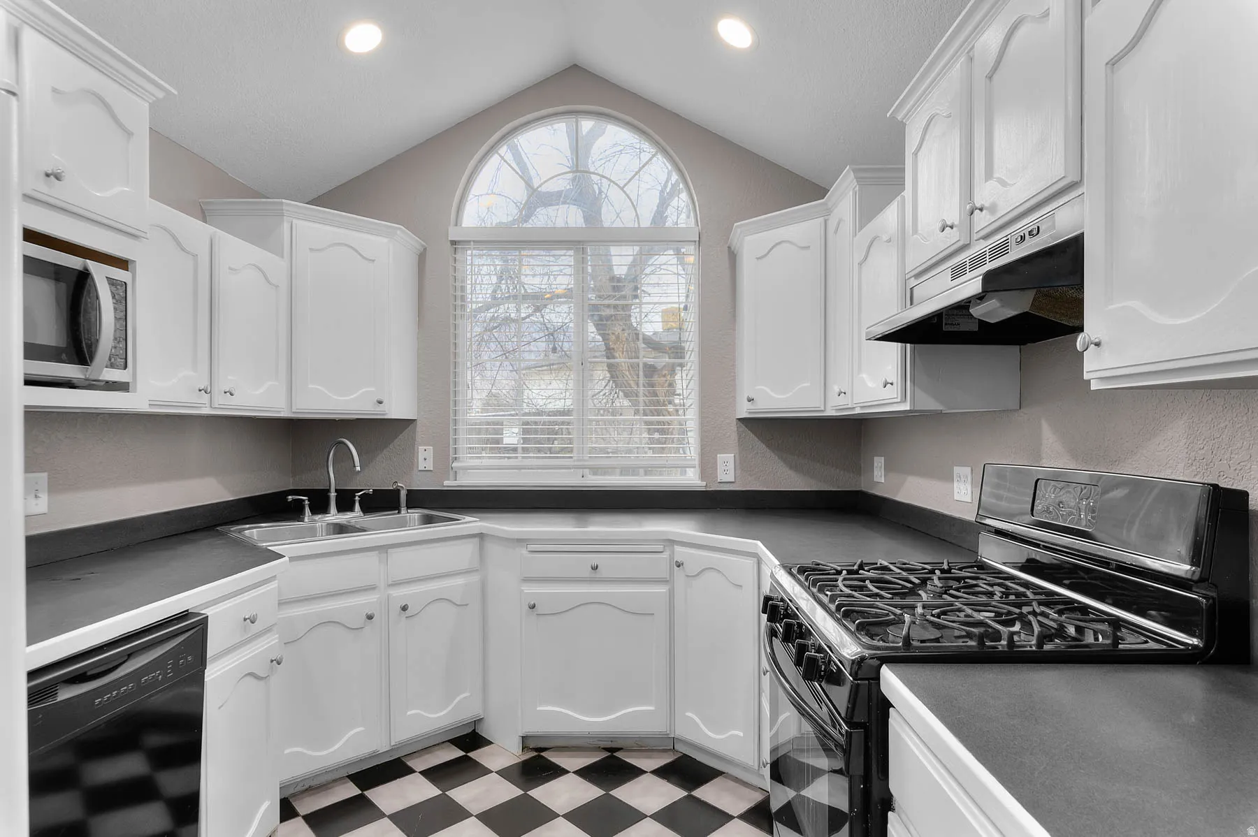Kitchen featuring gas stove, dark countertops, light flooring, dishwasher, and a textured wall