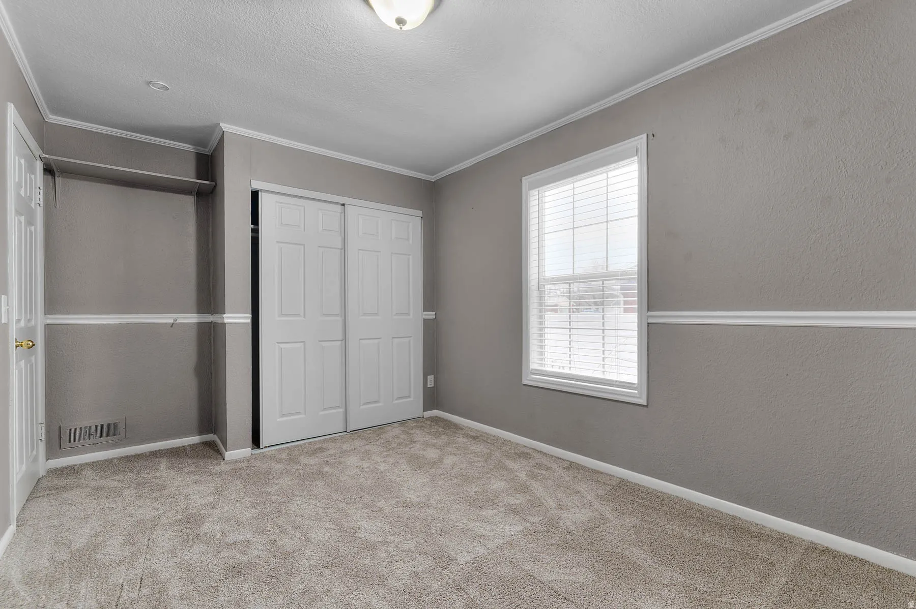 Unfurnished bedroom with a closet, light carpet, ornamental molding, a textured wall, and a textured ceiling
