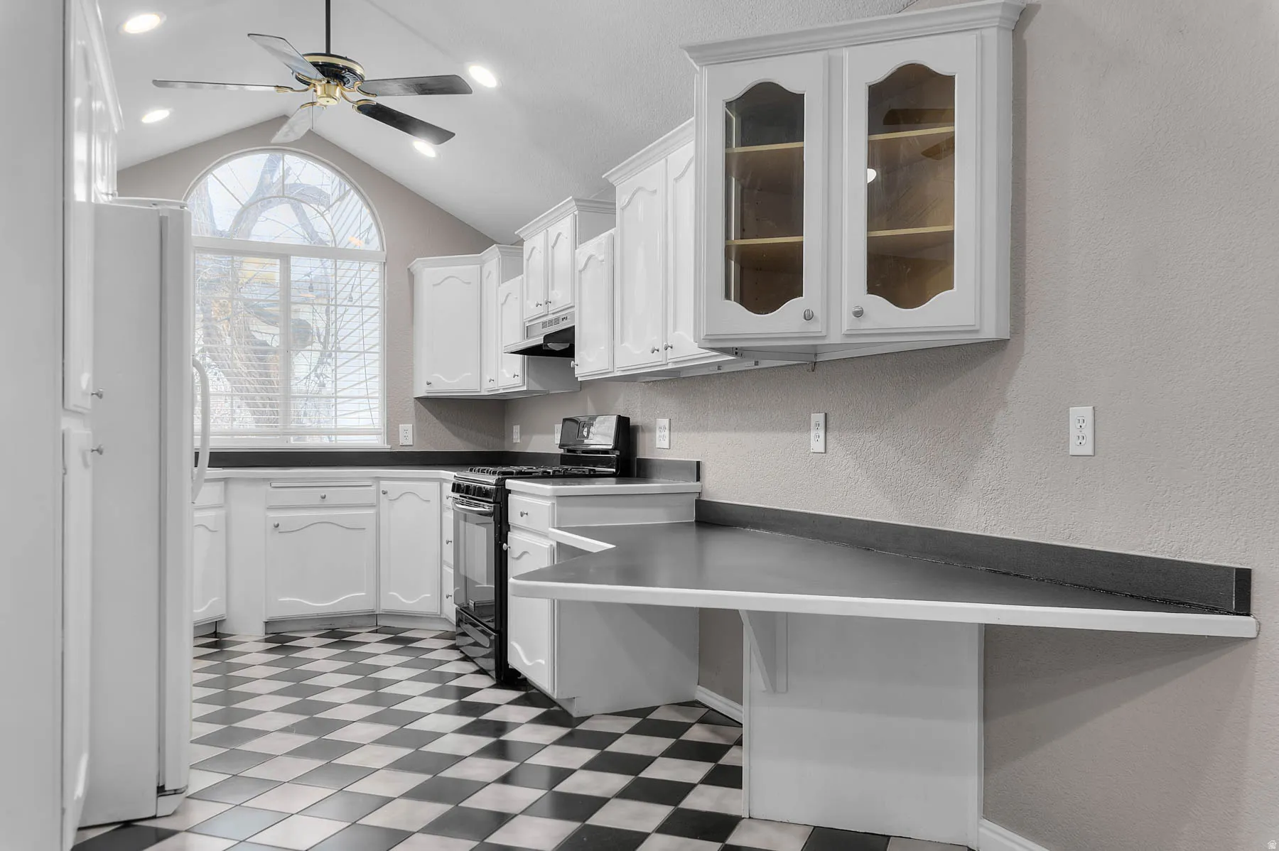 Kitchen with dark countertops, dark floors, black range with gas cooktop, a textured wall, and freestanding refrigerator