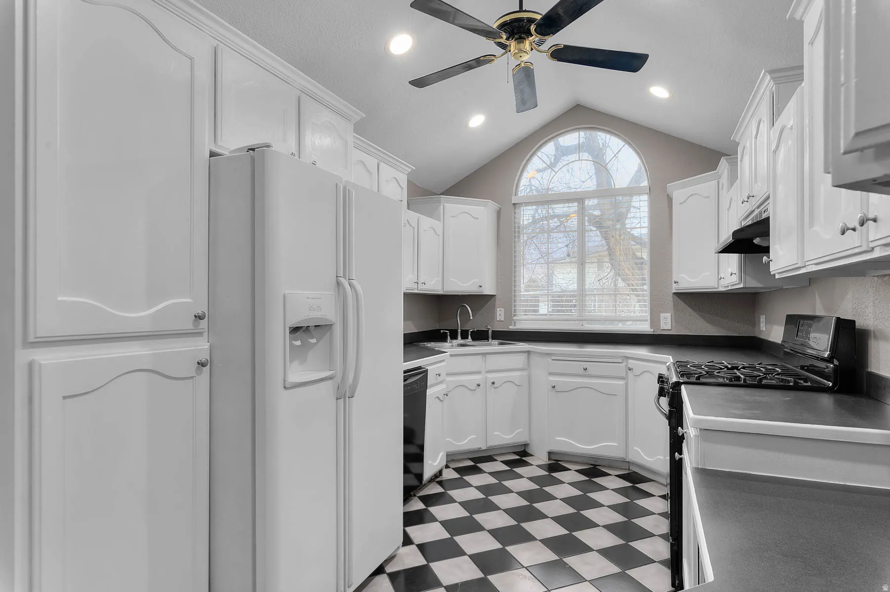 Kitchen featuring stainless steel range with gas stovetop, white fridge with ice dispenser, light floors, white cabinets, and recessed lighting