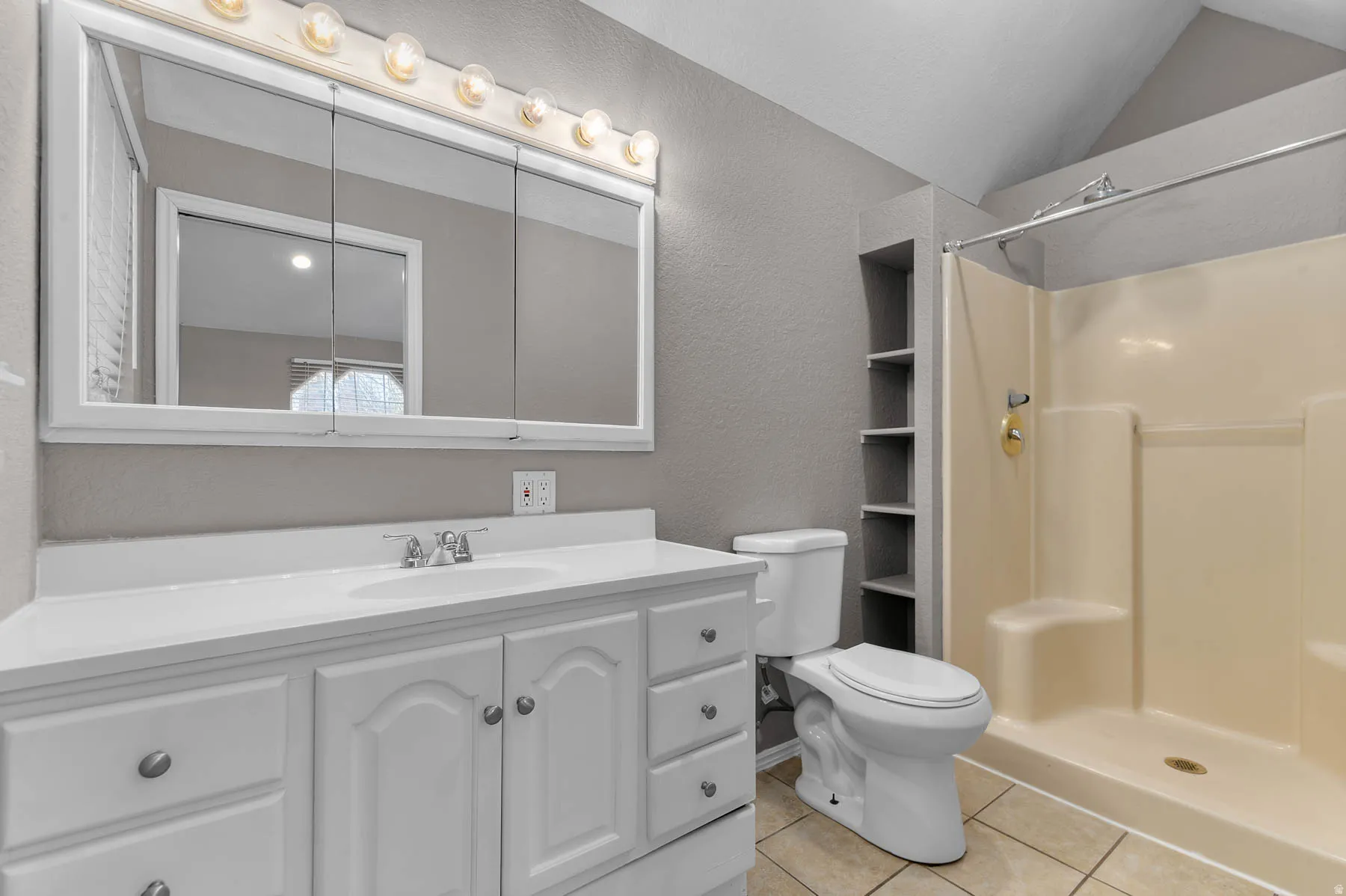Full bath with a textured wall, vanity, a stall shower, light tile patterned flooring, and vaulted ceiling