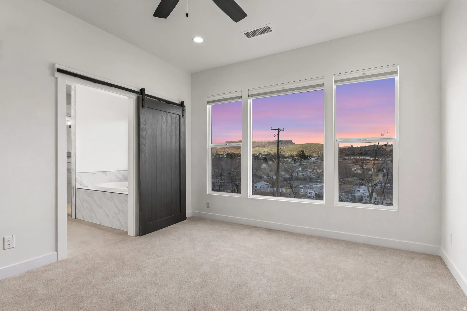 Unfurnished bedroom featuring a barn door, light carpet, a ceiling fan, ensuite bath, and recessed lighting