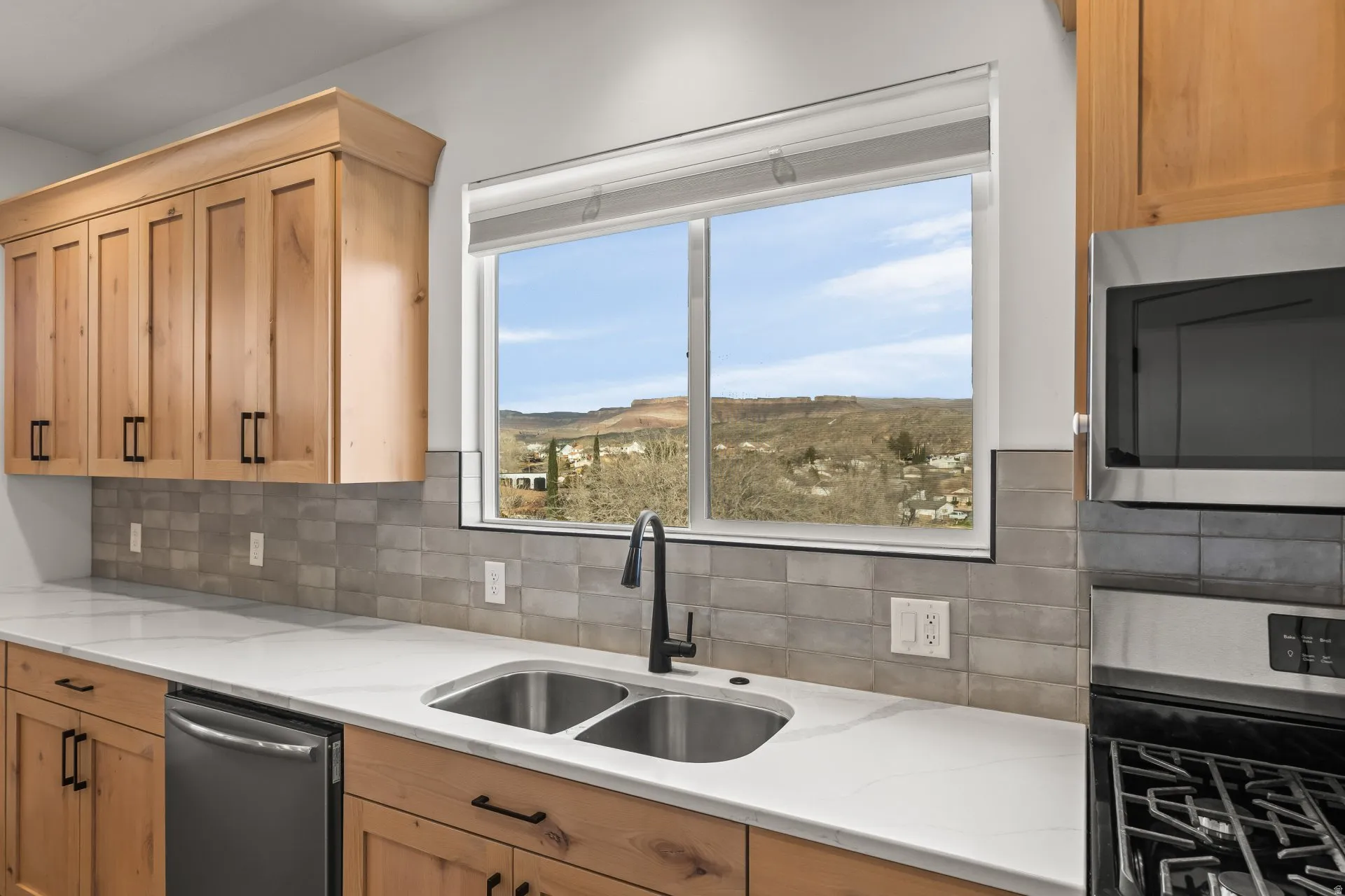 Kitchen featuring stainless steel appliances, backsplash, light wood finish cabinets, light stone counters, and a mountain view