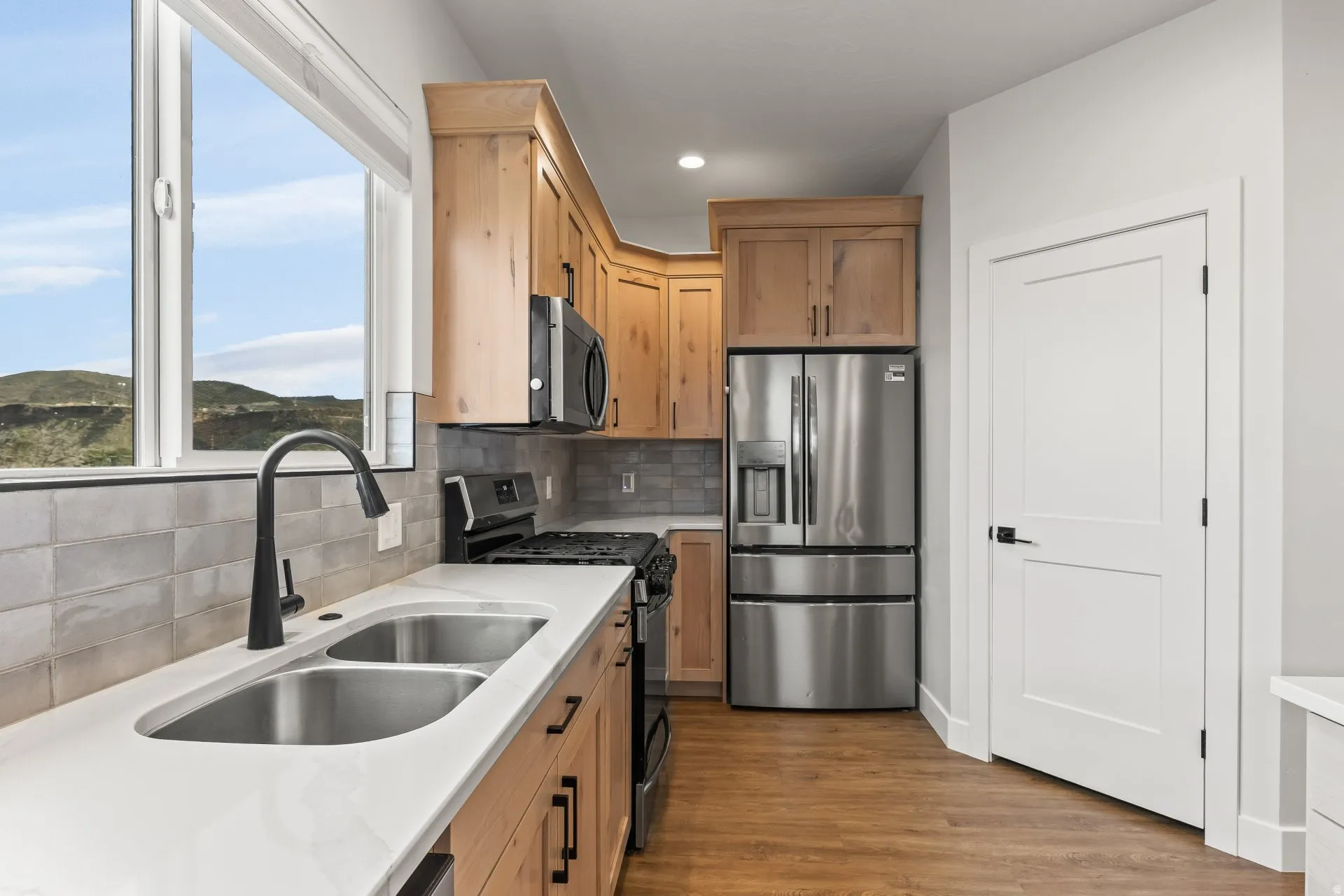 Kitchen featuring stainless steel appliances, backsplash, light wood-type flooring, light stone counters, and recessed lighting