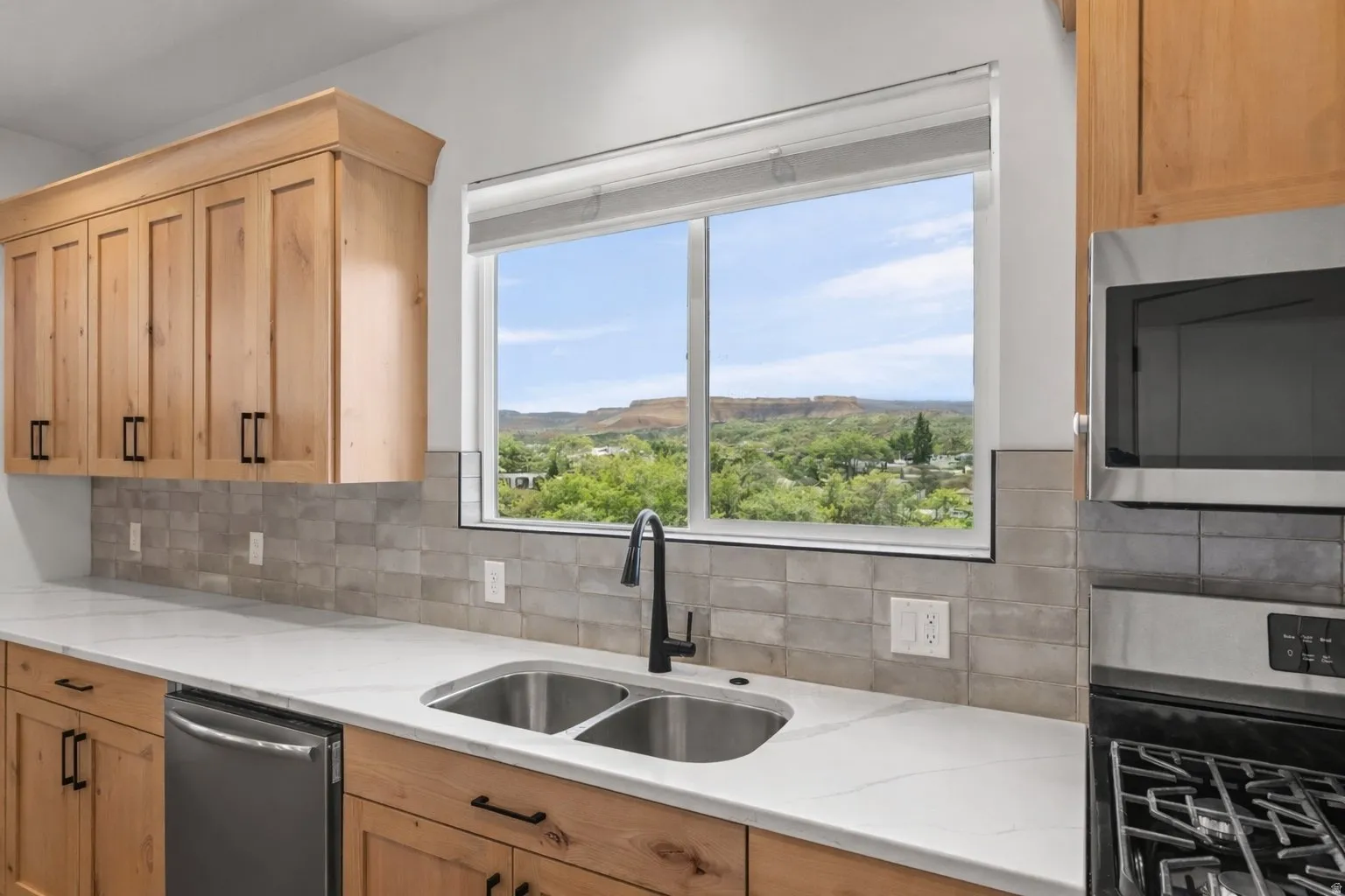 Kitchen with stainless steel appliances, light wood finish cabinetry, light stone countertops, and tasteful backsplash
