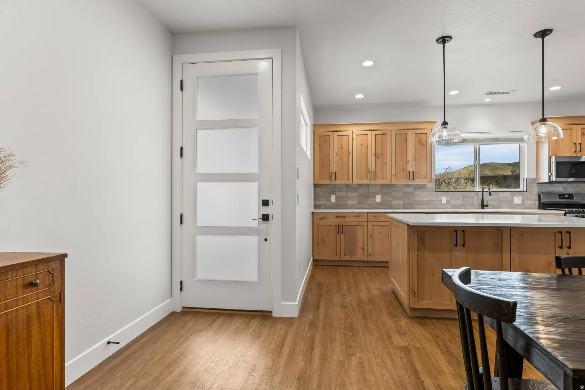 Kitchen featuring tasteful backsplash, light wood-style flooring, decorative light fixtures, stainless steel appliances, and light stone countertops