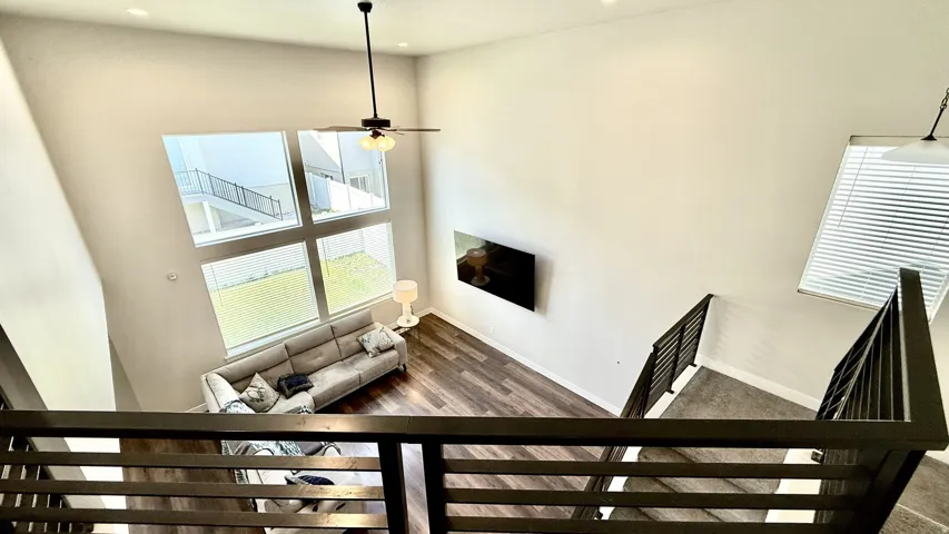 Two-story living area featuring wood-finish flooring, a contemporary ceiling fan, and large windows