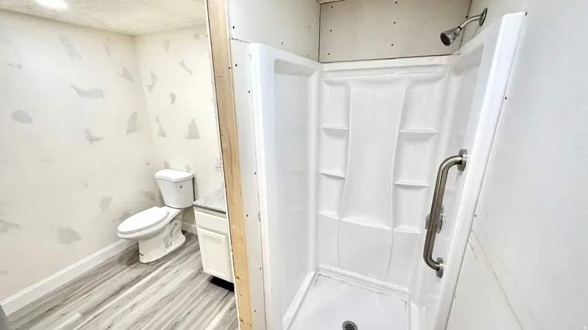 White shower stall with an integrated grab bar and chrome showerhead, complemented by wood-finish flooring