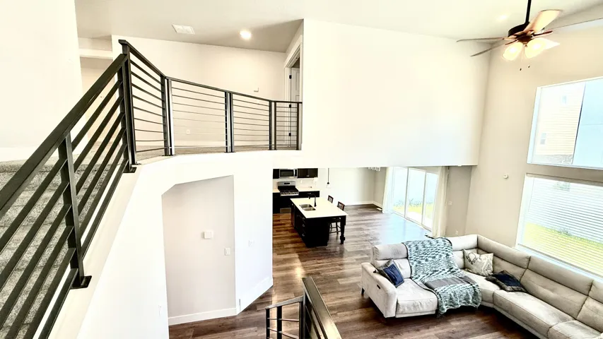 Open concept living area featuring a two-story ceiling, wood-finish flooring, and a modern horizontal metal railing system