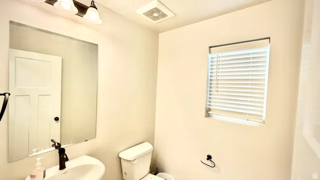 Powder room featuring a pedestal sink with a dark bronze faucet, wall-mounted mirror, white horizontal blinds, and a traditional toilet