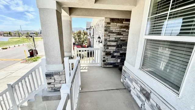 Inviting front porch featuring stone veneer accents, stucco siding, white railings, and an exterior wall lantern