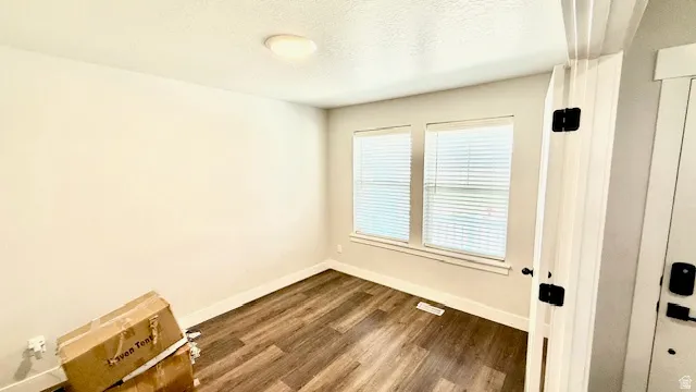 Interior room featuring wood-finish flooring, neutral wall tones, and two windows equipped with blinds