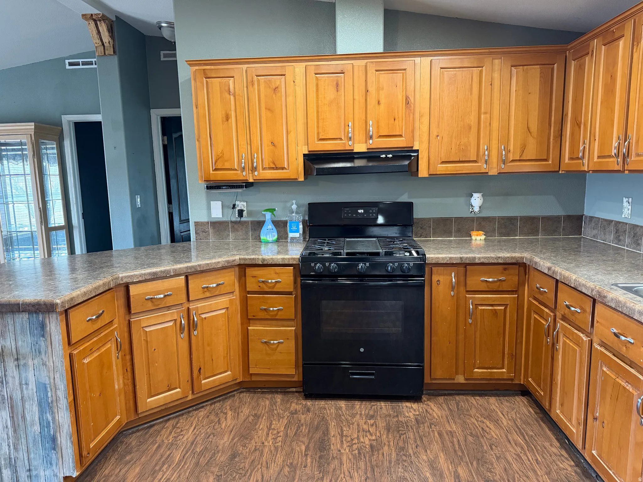 Kitchen with lofted ceiling, black range with gas stovetop, wood finish cabinetry, and a peninsula