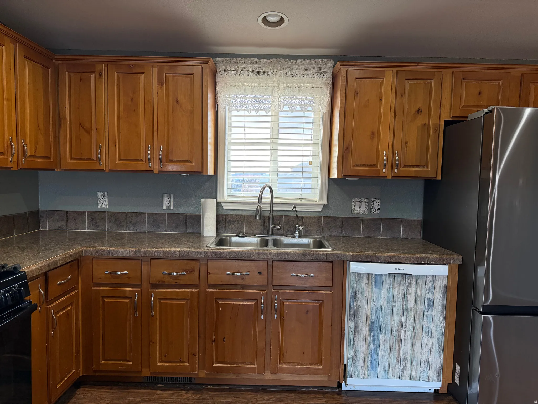 Kitchen featuring dishwasher, dark countertops, wood finish cabinets, freestanding refrigerator, and recessed lighting