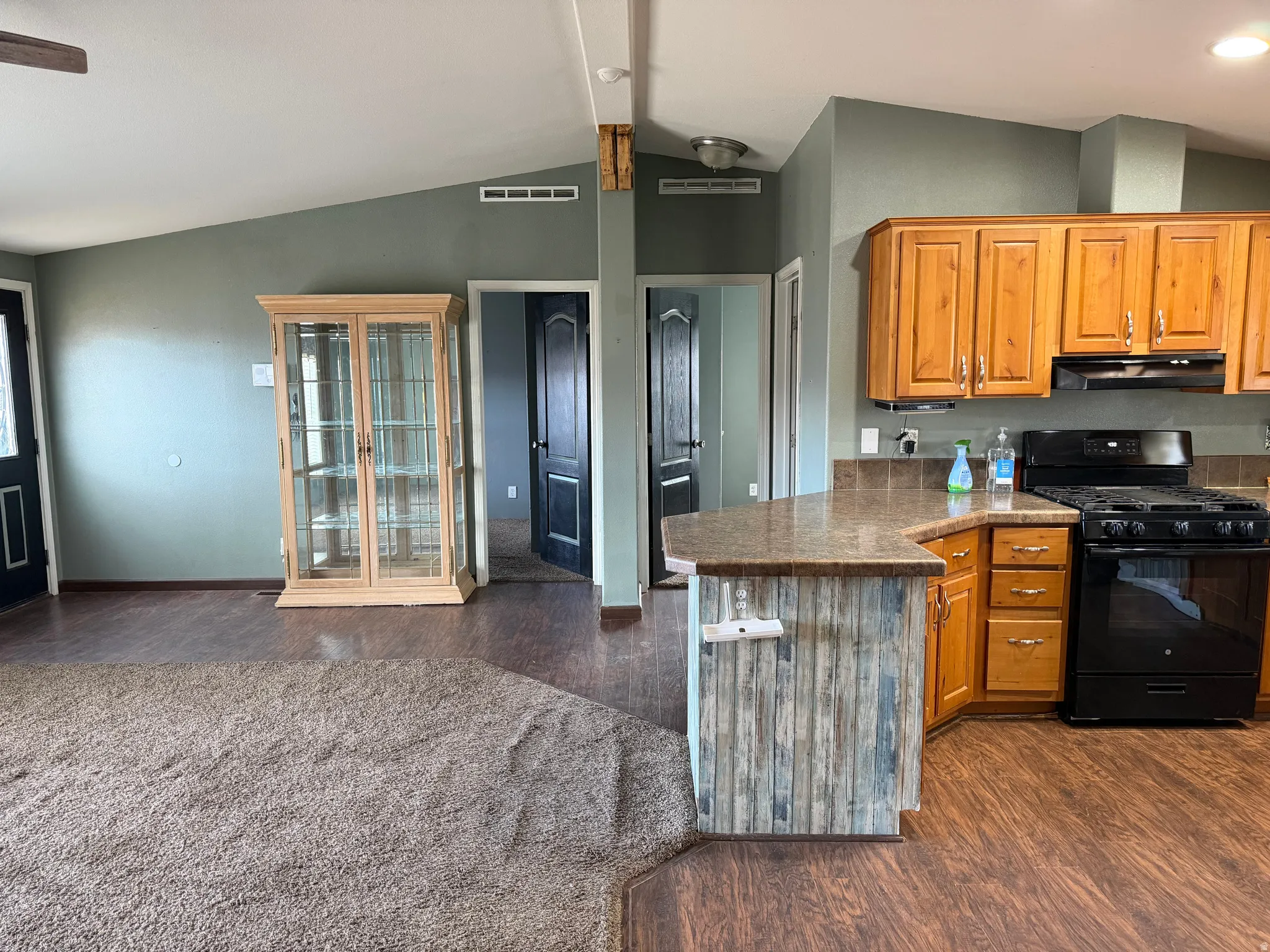 Kitchen featuring black range with gas stovetop, a peninsula, wood finish cabinets, dark wood finished floors, and beamed ceiling