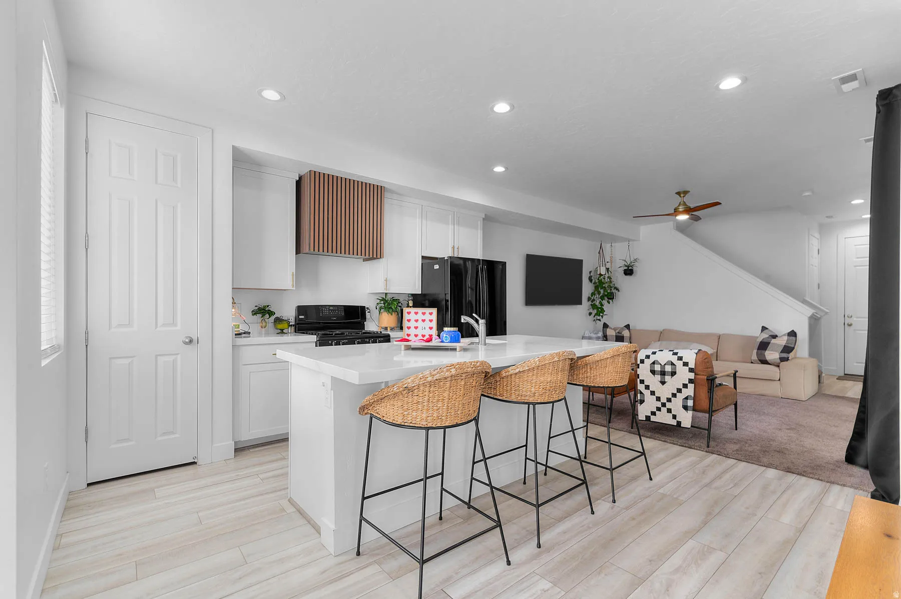 Kitchen featuring recessed lighting, a kitchen breakfast bar, white cabinetry, black appliances, and light wood-style flooring