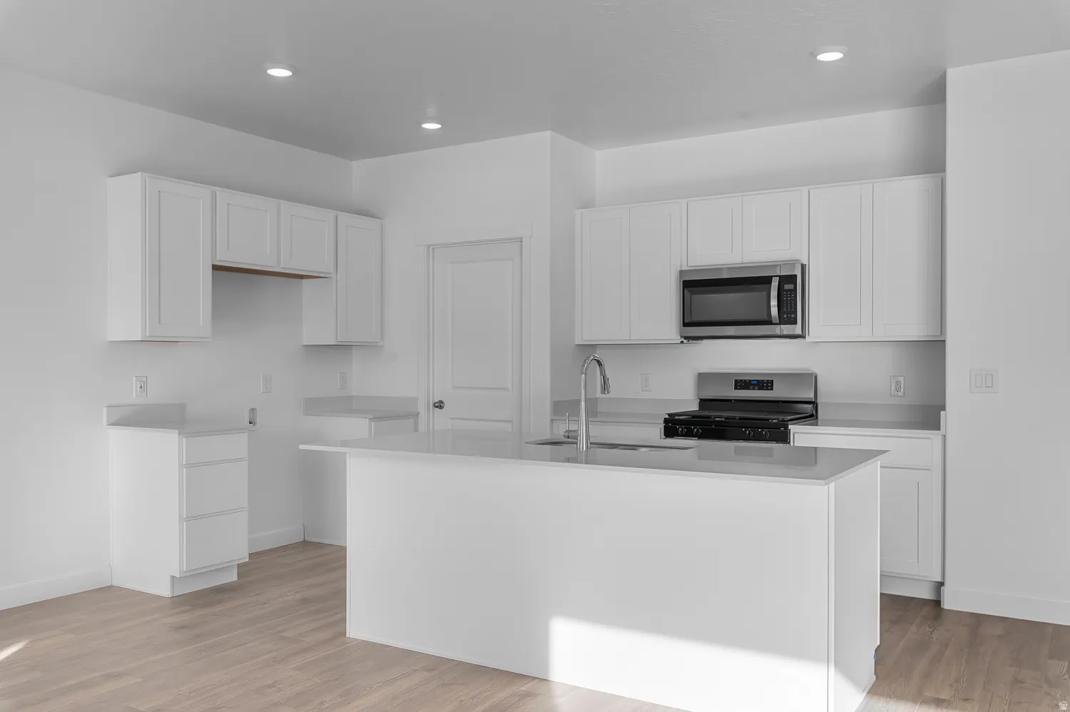Kitchen with white cabinetry, range, a kitchen island with sink, stainless steel microwave, and light wood finished floors