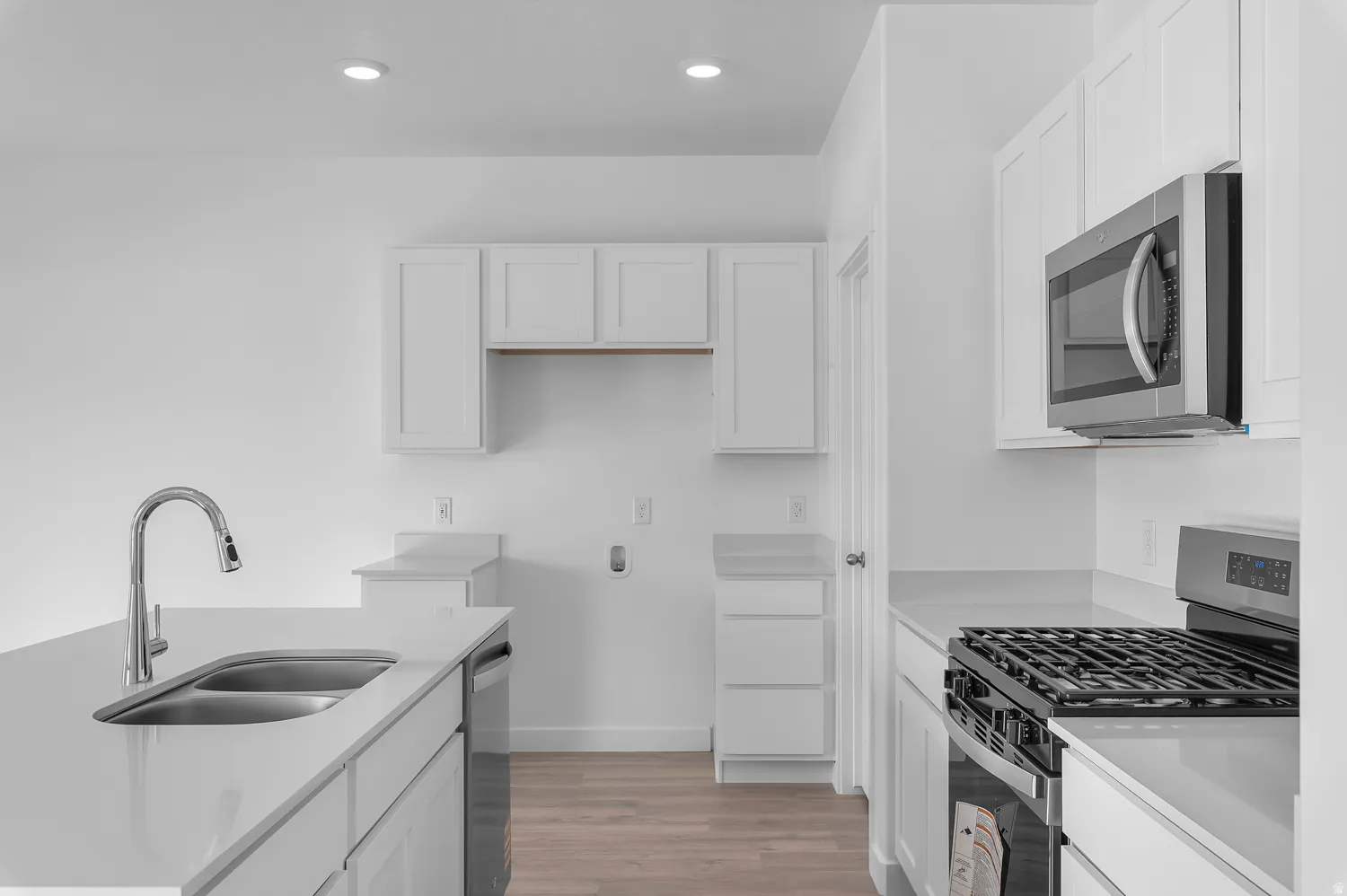 Kitchen with stainless steel appliances, white cabinets, light wood finished floors, light stone countertops, and recessed lighting
