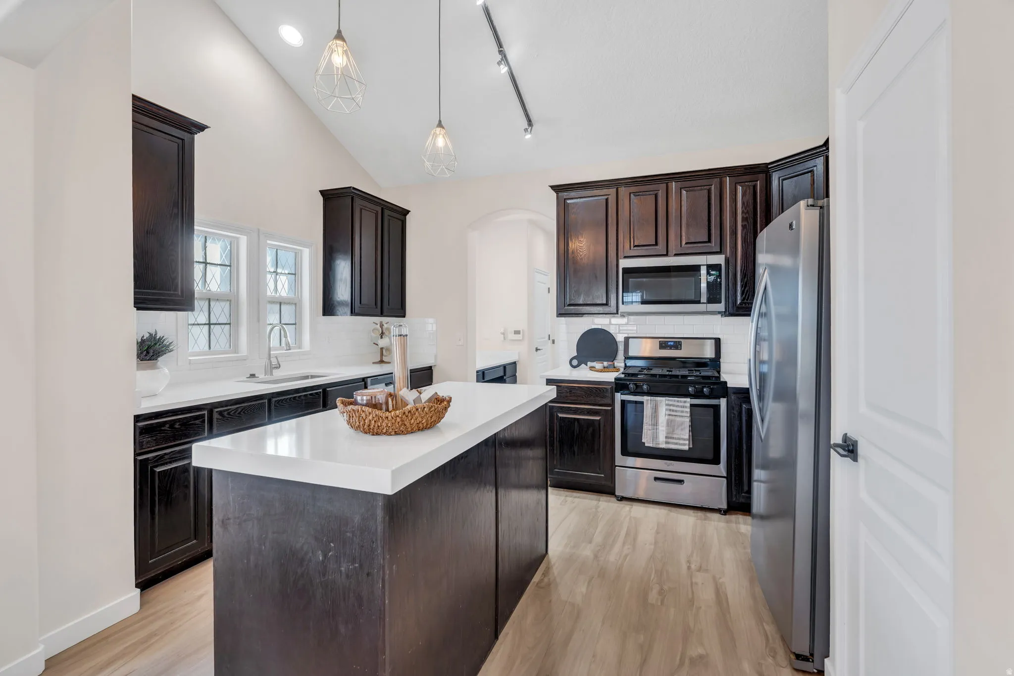 Kitchen with stainless steel appliances, dark wood finish cabinets, lofted ceiling, light countertops, and decorative backsplash