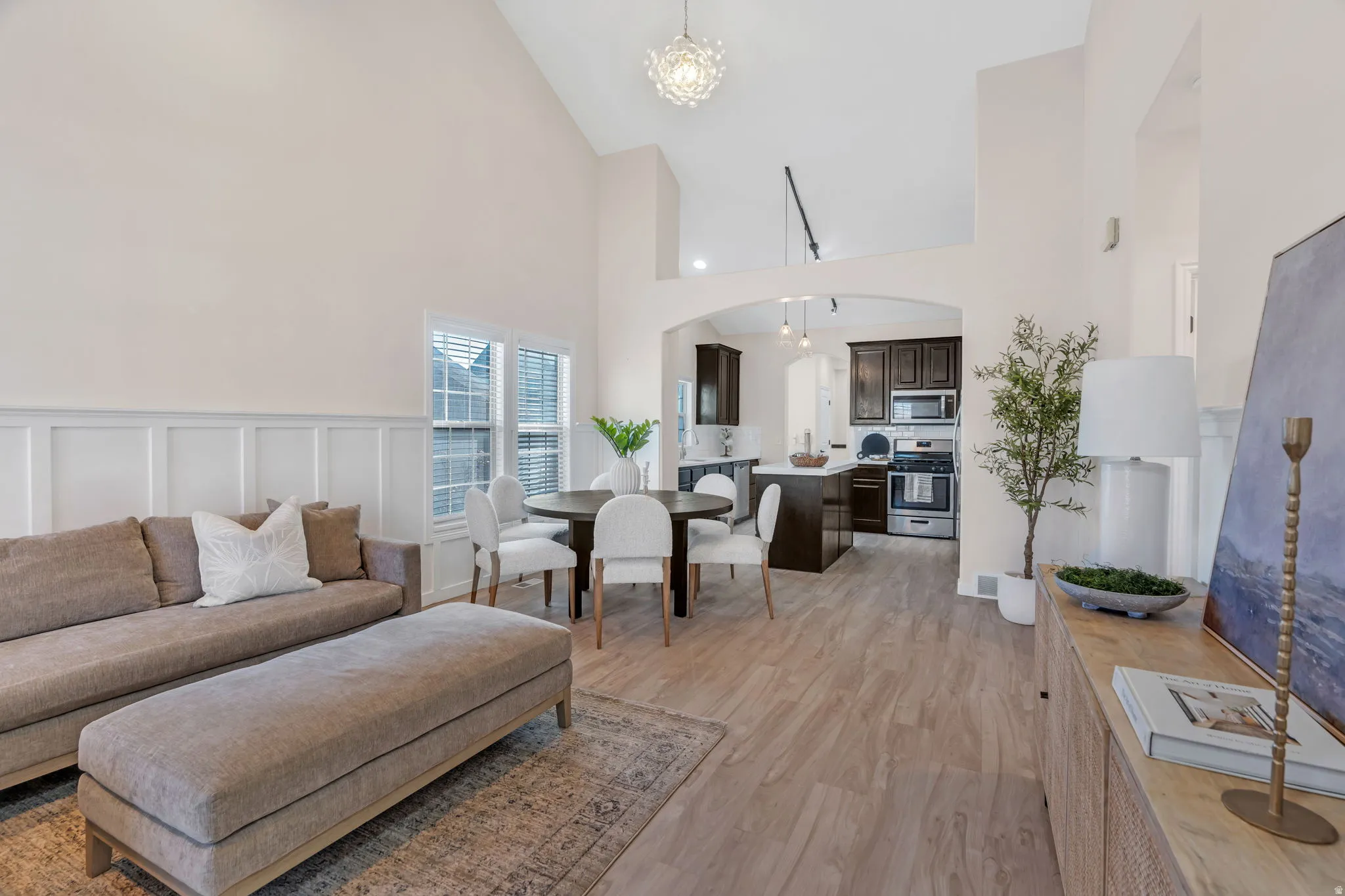 Living area with hanging lights, arched walkways, light wood-type flooring, lofted ceiling, and a decorative wall