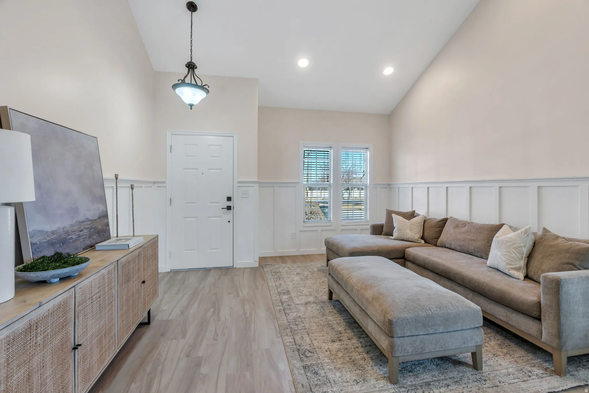 Living area with lofted ceiling, a wainscoted wall, a decorative wall, and light wood-style floors