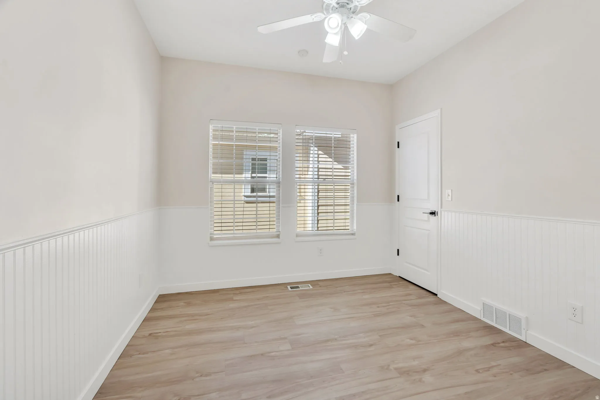 Empty room with light wood-style floors, a ceiling fan, and wainscoting