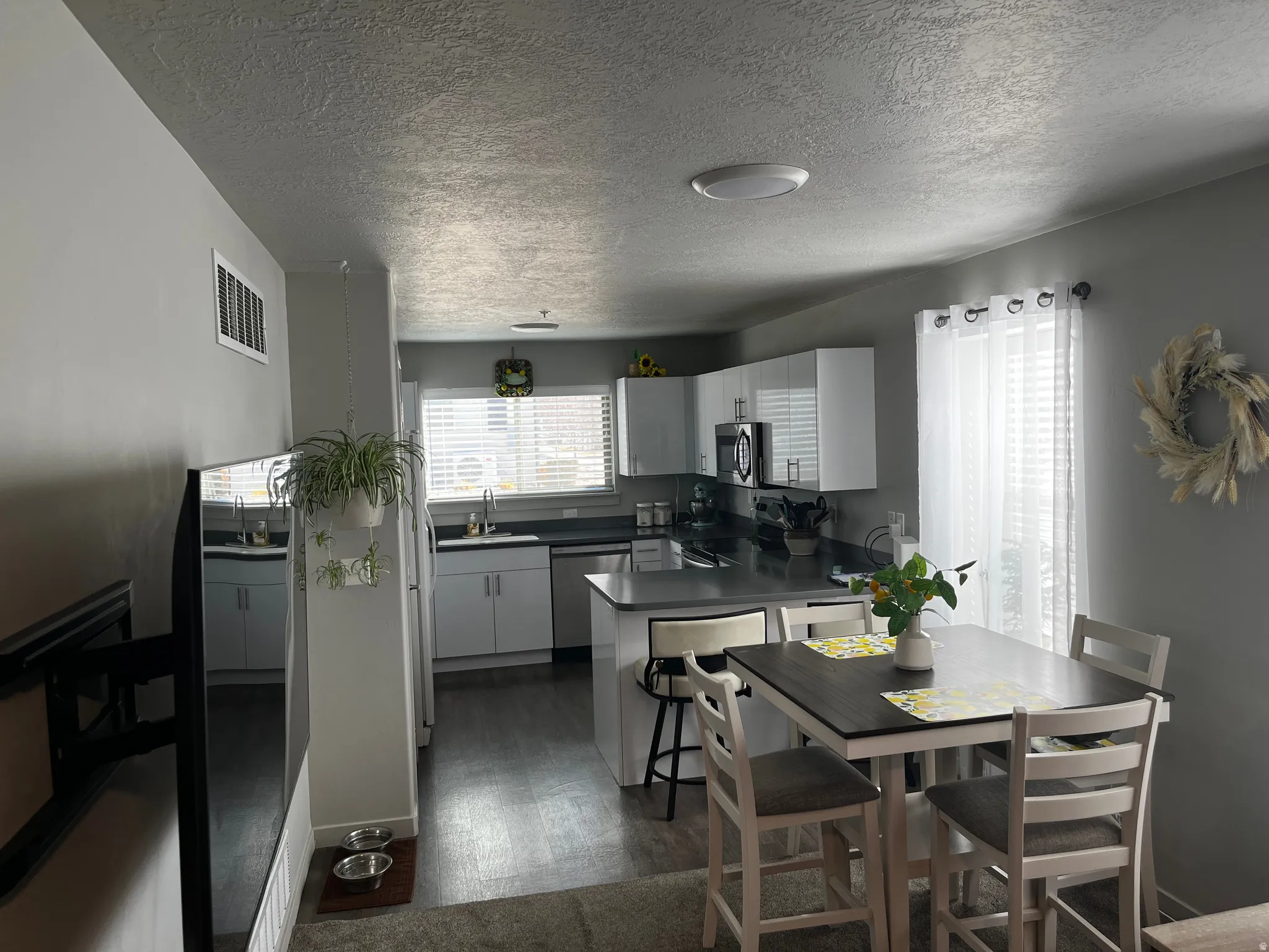 Kitchen featuring dark countertops, a peninsula, appliances with stainless steel finishes, white cabinetry, and dark wood-style floors