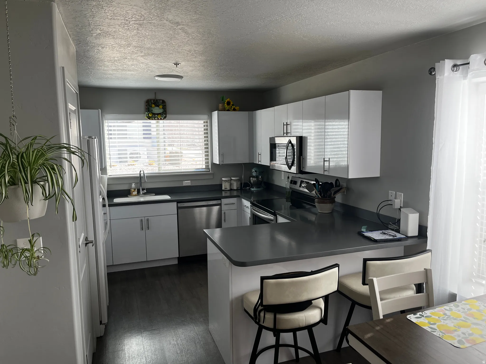Kitchen with a peninsula, white cabinetry, stainless steel appliances, dark wood finished floors, and a textured ceiling