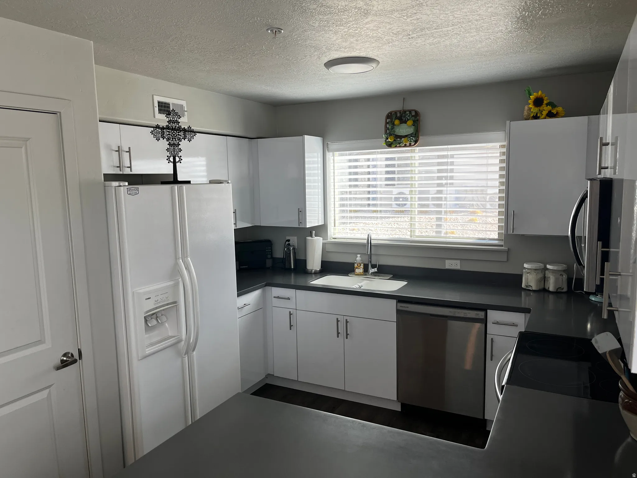 Kitchen featuring dark countertops, appliances with stainless steel finishes, white cabinets, and a textured ceiling