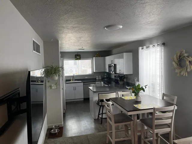 Kitchen featuring dark countertops, a peninsula, appliances with stainless steel finishes, white cabinetry, and dark wood-style floors