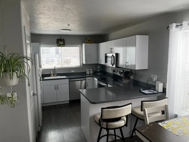 Kitchen with a peninsula, white cabinetry, stainless steel appliances, dark wood finished floors, and a textured ceiling
