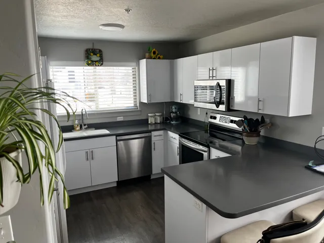 Kitchen with appliances with stainless steel finishes, a peninsula, a breakfast bar area, white cabinets, and a textured ceiling