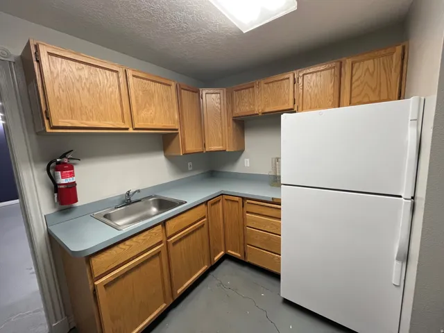 Kitchen with freestanding refrigerator, light countertops, a textured ceiling, wood finish cabinets, and finished concrete flooring