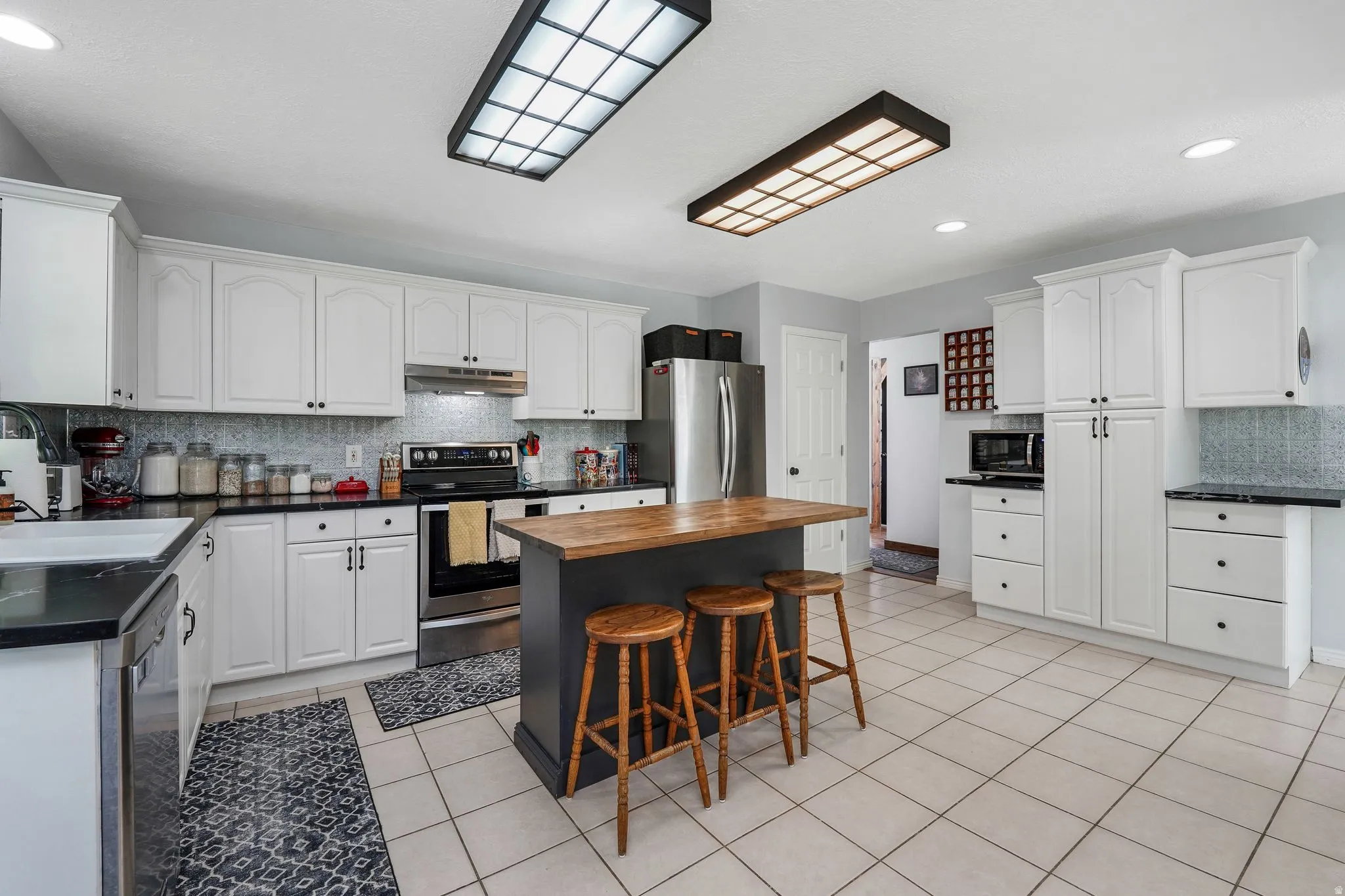 Kitchen with tasteful backsplash, stainless steel appliances, a breakfast bar area, white cabinetry, and recessed lighting