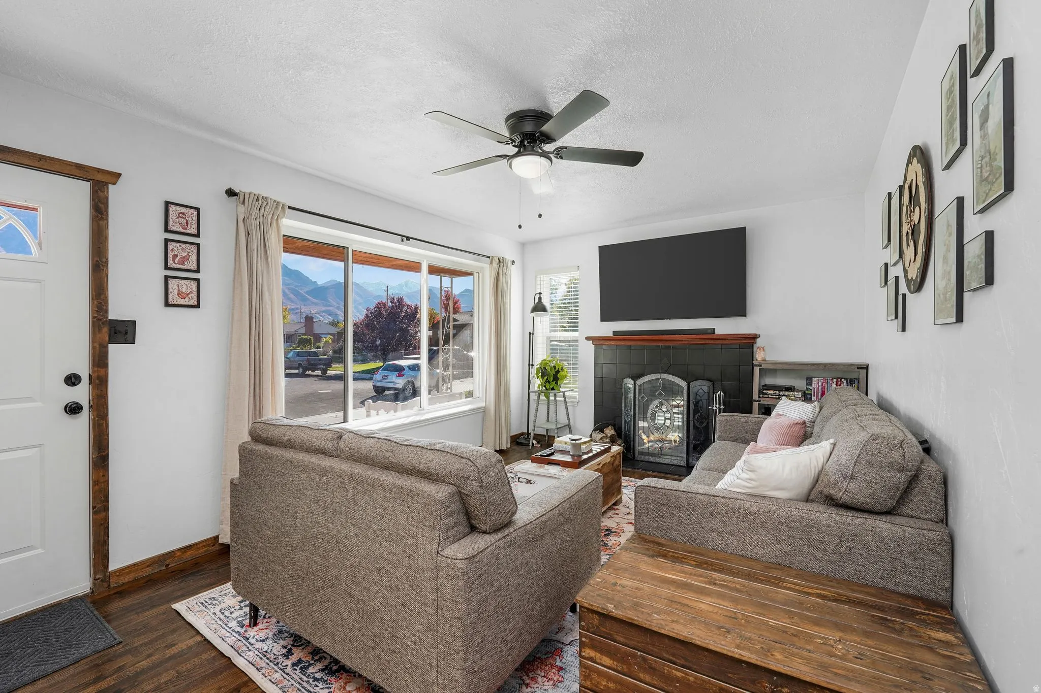 Living area featuring a fireplace, dark wood finished floors, a textured ceiling, and ceiling fan