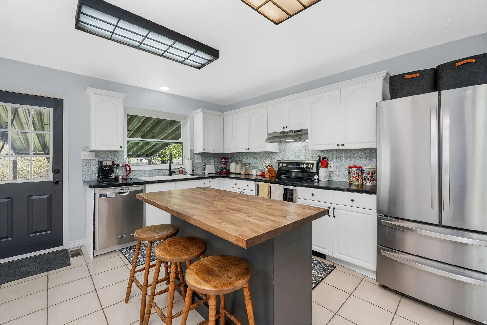 Kitchen featuring stainless steel appliances, a breakfast bar, butcher block counters, light tile patterned floors, and a kitchen island